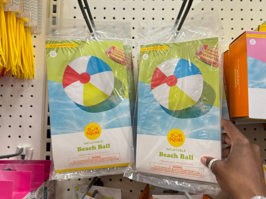 hand reaching for a multi color inflatable beach ball in packaging on a shelf