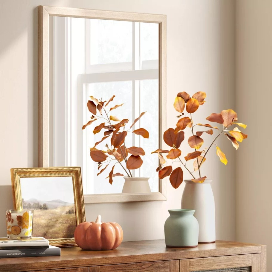 natural wood framed wall mirror above a console table with fall decor