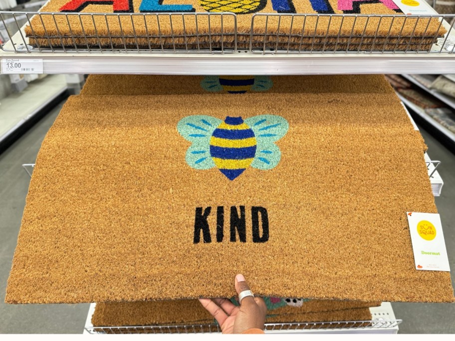 hand holding a coir doormat with a bumble bee that says "Kind"