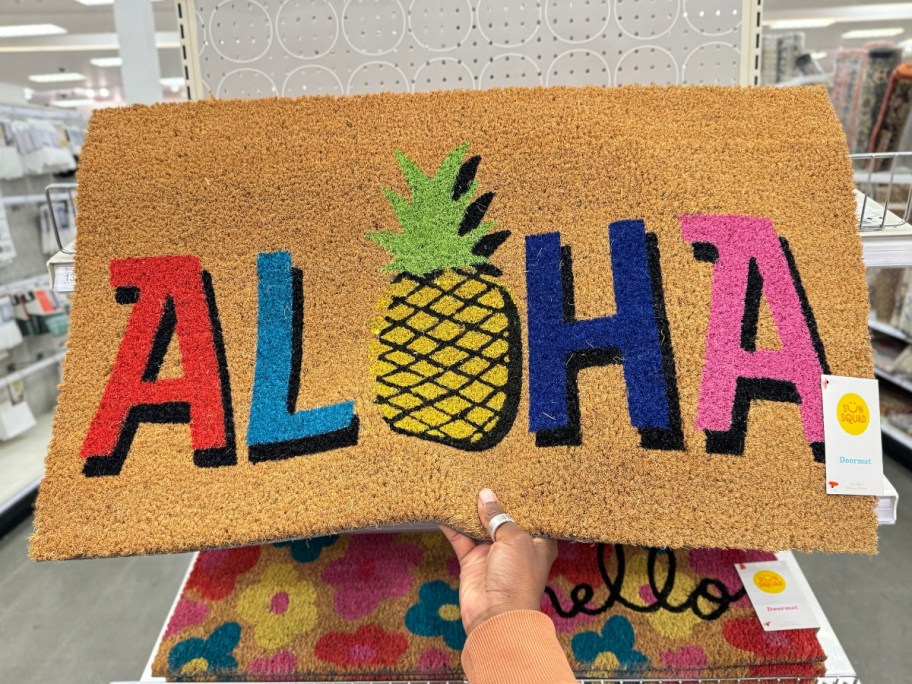 hand holding a coir doormat with "Aloha" and a pineapple on it