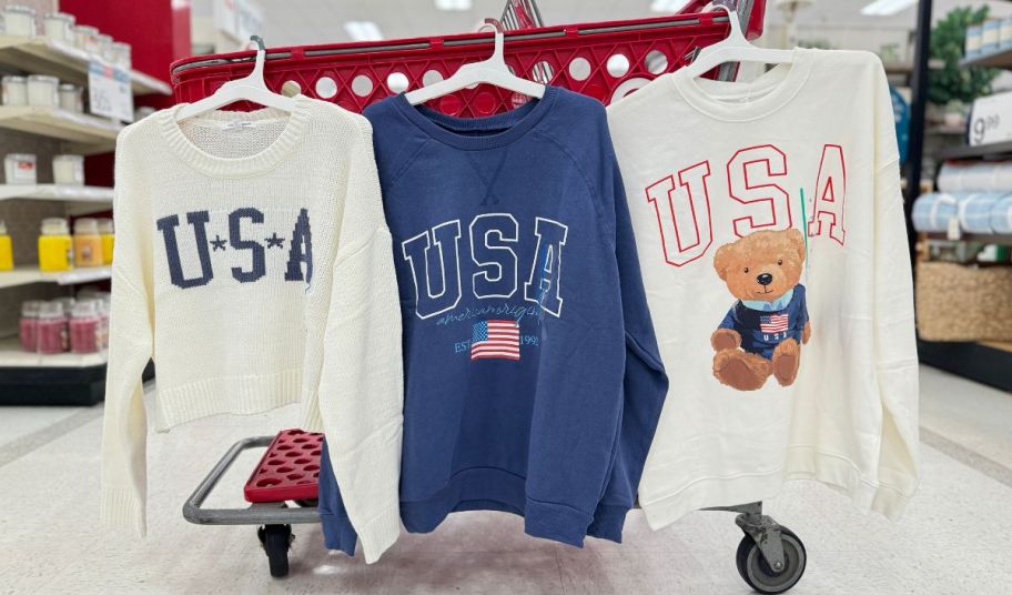 3 womens USA tops hanging on the side of a shopping cart in a target store