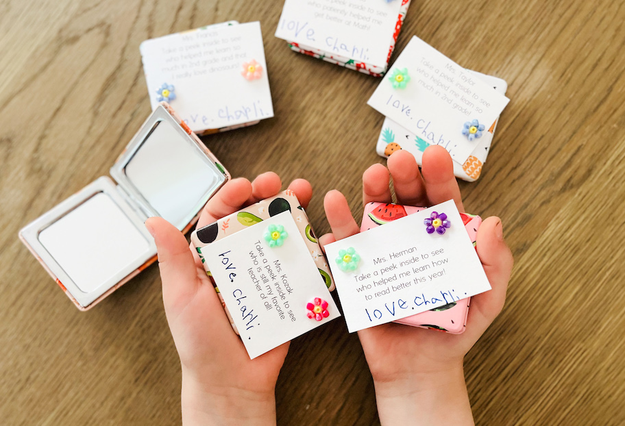 childs hands holding notes to teachers with fruit themed compact mirrors