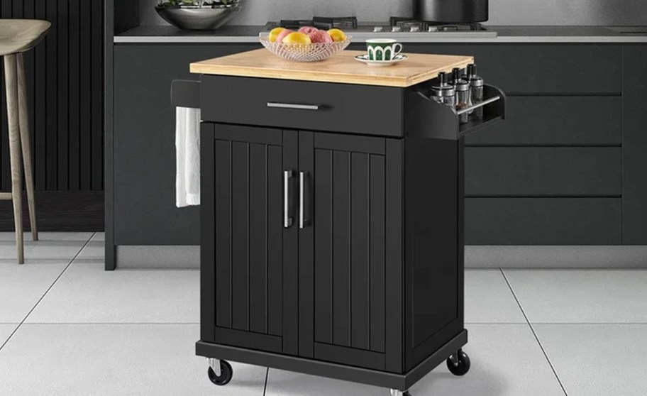 black kitche island with wood top in kitchen with bowl of fruit