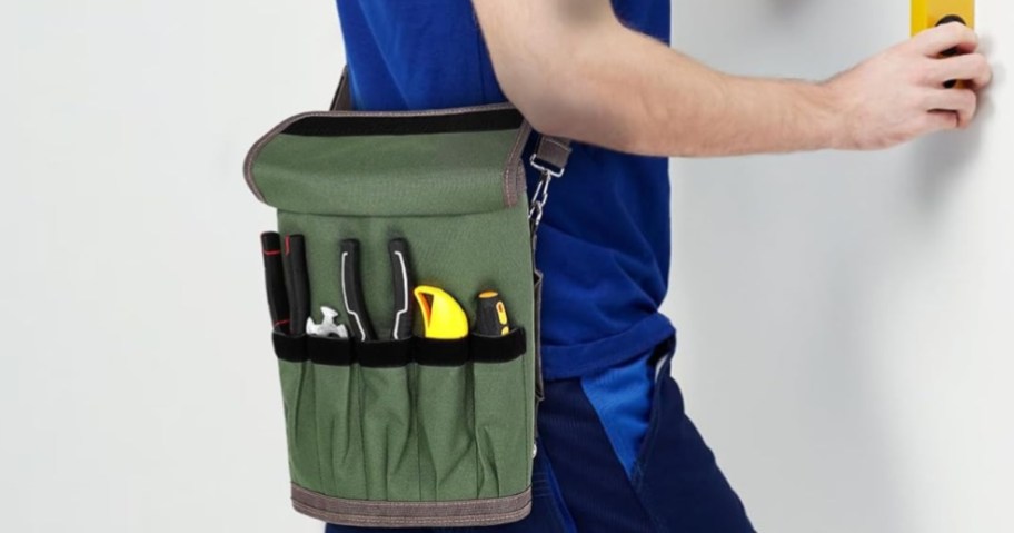 Green tool bag organizer hanging on a man's shoulder that is working on a wall.