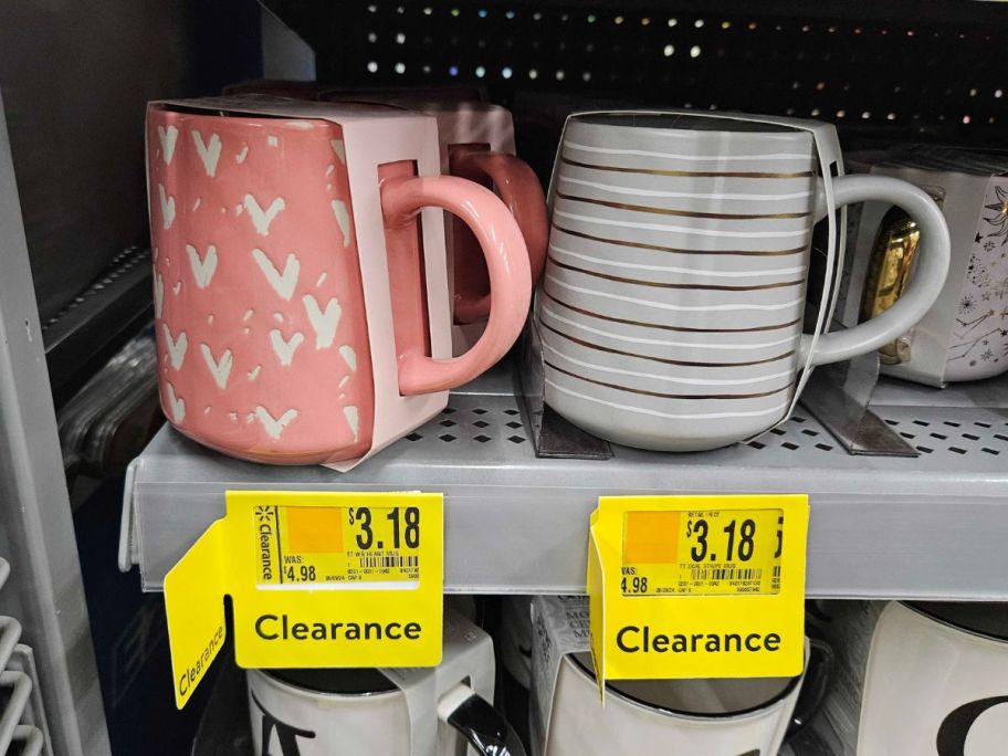 a pink mug with white hearts and a white, silver and gold striped mug on a store shelf