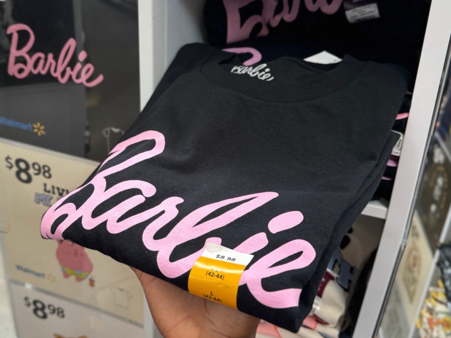 hand reaching for a black and pink Barbie t-shirt from a display at Walmart