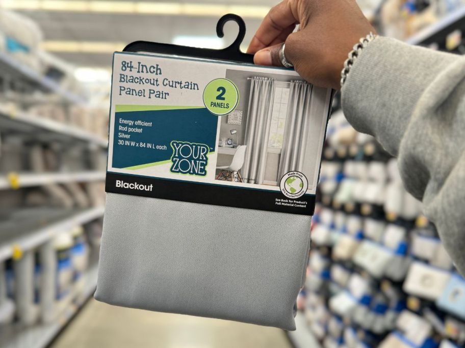 walmart Your Zone Solid Blackout Rod Pocket Curtain Panel Pair in silver being held by hand in aisle at store