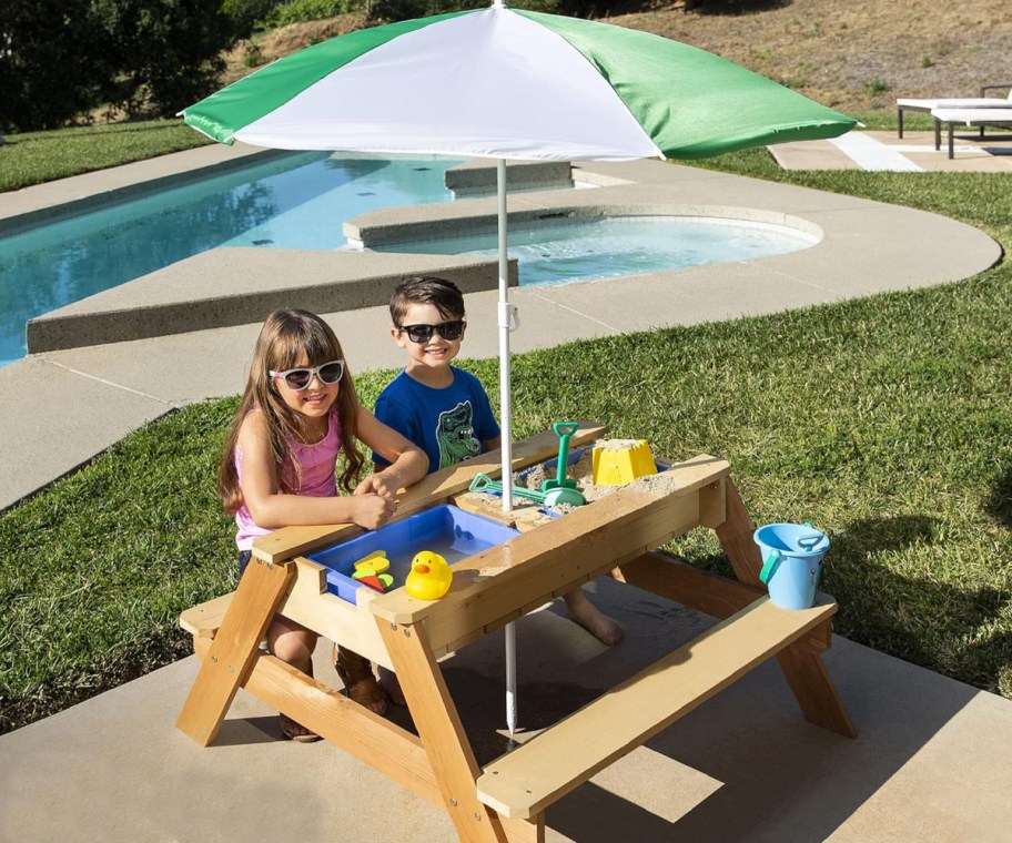 kids sitting at bench water table with umbrella