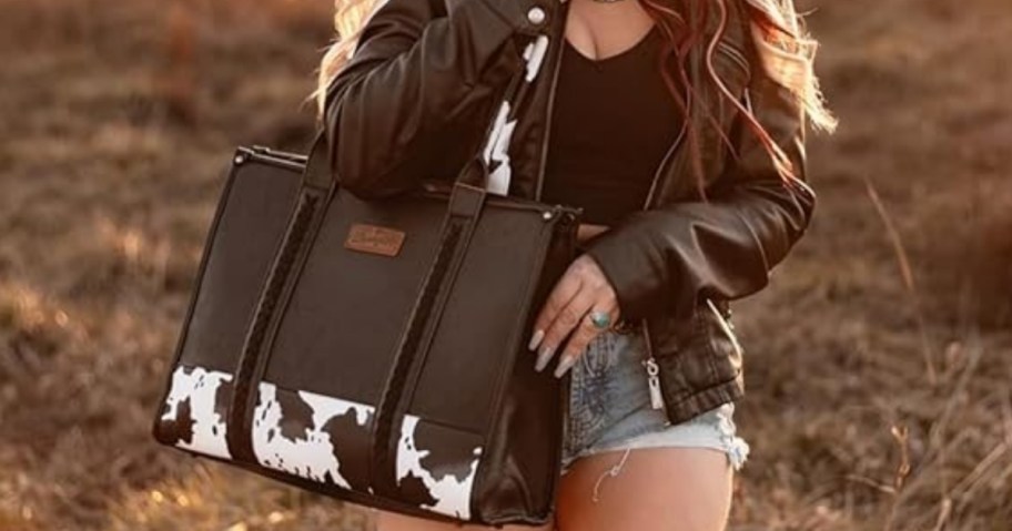 woman carrying a large black Wrangler tote bag with cow print details