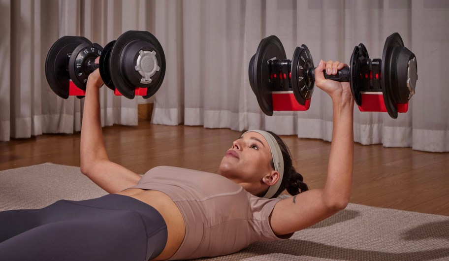 woman laying down in tan shirt holding two dumbbells
