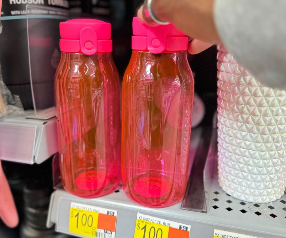 a womans hand grabbing a water bottle from a store shelf