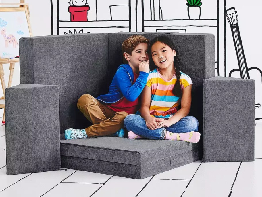 little boy and girl talking and sitting on a grey play couch with separate cushions set up like a fort