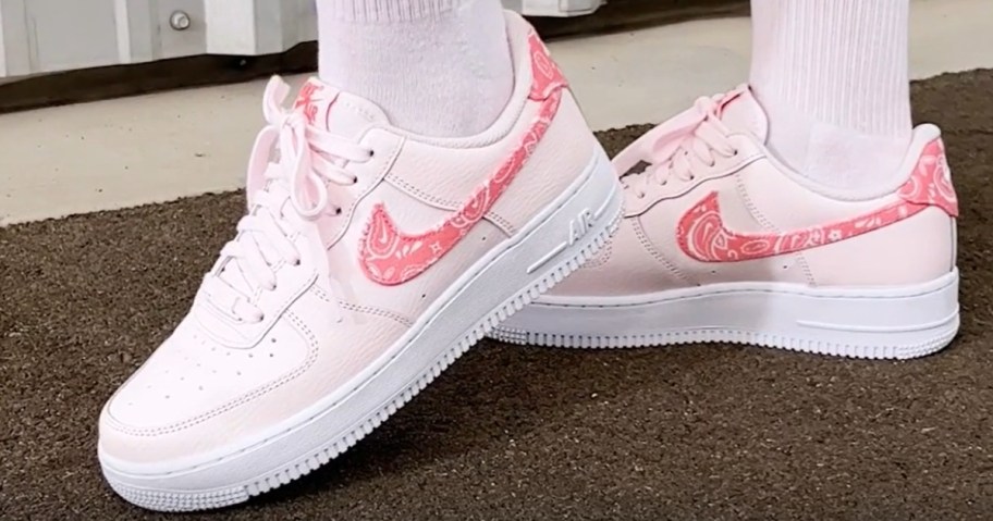 women's feet wearing light pink Nike Air Force 1 shoes with a darker pink paisley swoosh