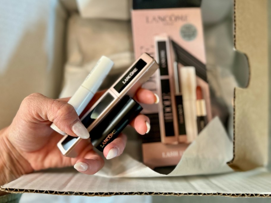 hand holding Lancome makeup items with a box with more items behind it