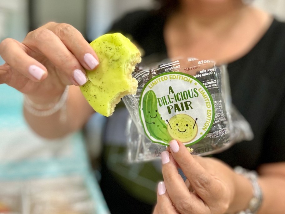 hand holding a Dill Pickle cookie with a couple bites taken out in one hand and the wrapper in their other hand