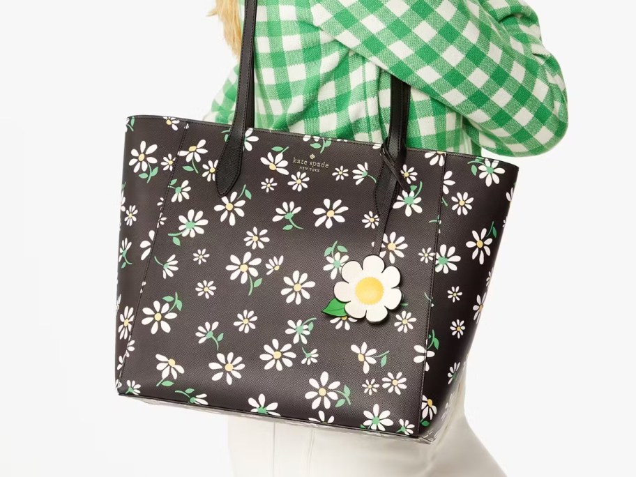 woman carrying a large Kate Spade tote in black with daisies on it