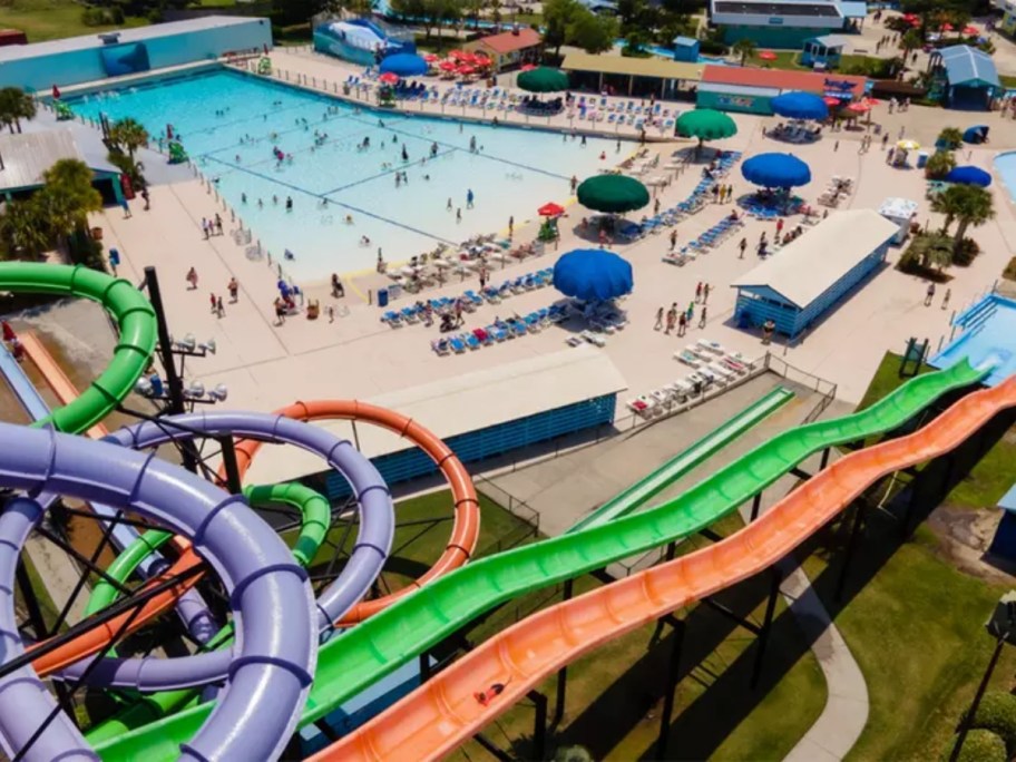 small waterpark with purple, green and orange waterslides and large swimming pools shown