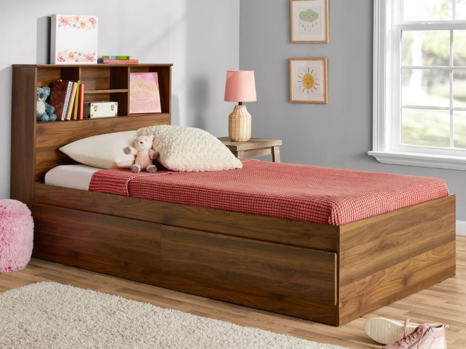 walnut color twin bed with storage headboard and pink blanket in a kids bedroom