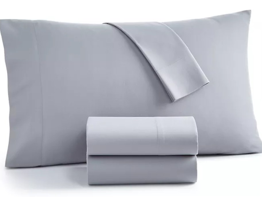 bed pillow with a grey pillowcase and folded grey sheet set in front of it