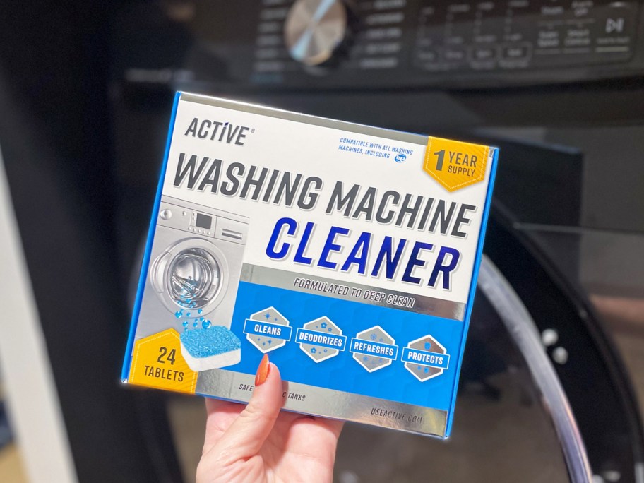 hand holding a box of Active Washing Machine Cleaner in front of washing machine