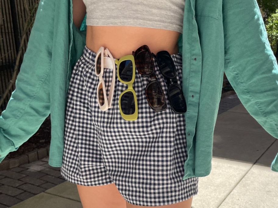 woman wearing 4 pairs of sunglasses hanging on the waist of her shorts
