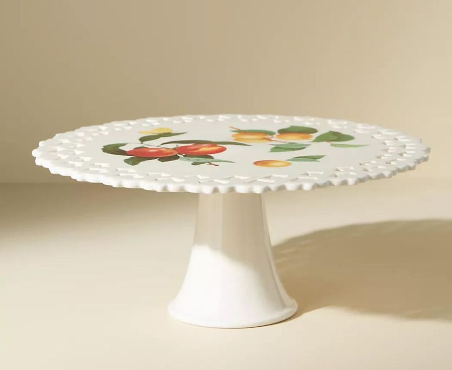 A white cake stand with fruit painted on it 