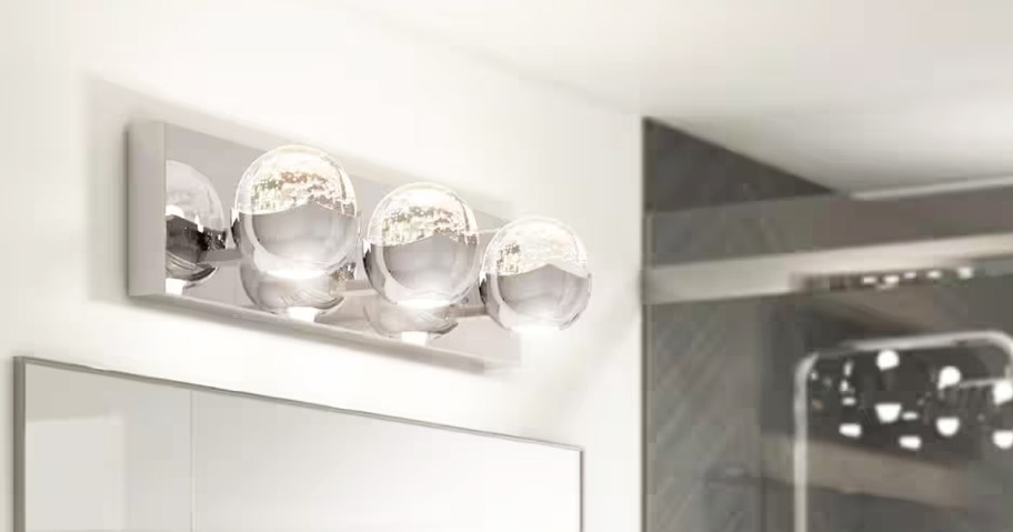 chrome vanity light with 3 glass lights on wall above mirror