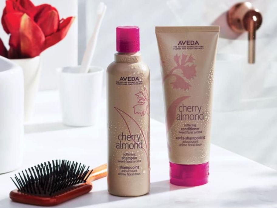 Bottles of Aveda Vherry Almond Shampoo and Conditoiner on a counter next to a hairbrush