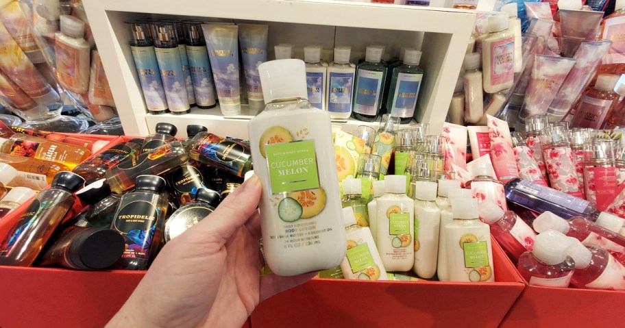hand holding up a cucumber melon body lotion with boxes of other scents behind