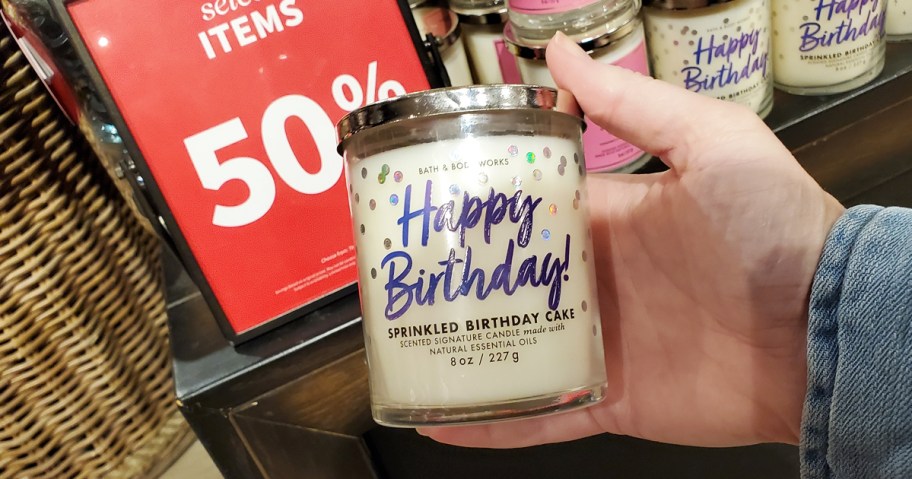 hand holding a white candle that says "happy birthday" on it
