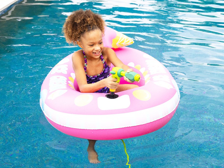 girl sitting in a pink pool float with water blaster