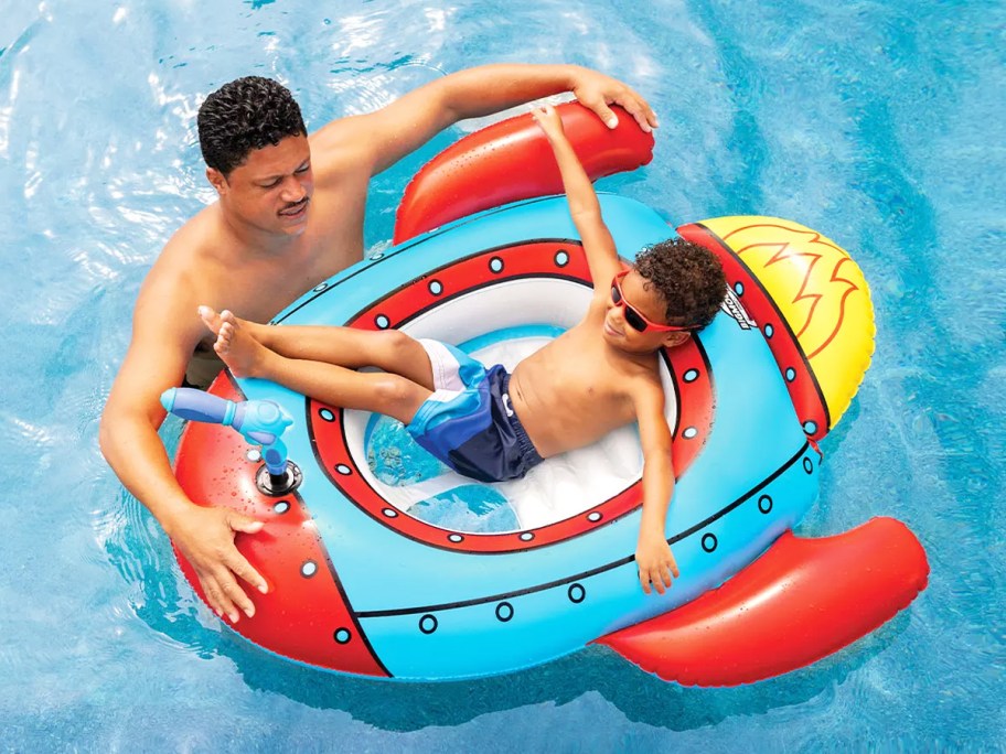 boy lounging in rocket ship pool float with dad hanging on sides