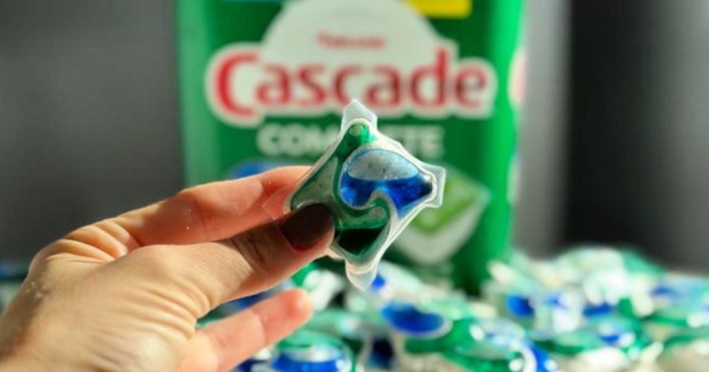 person holding dishwasher detergent pod in front of cascade complete container