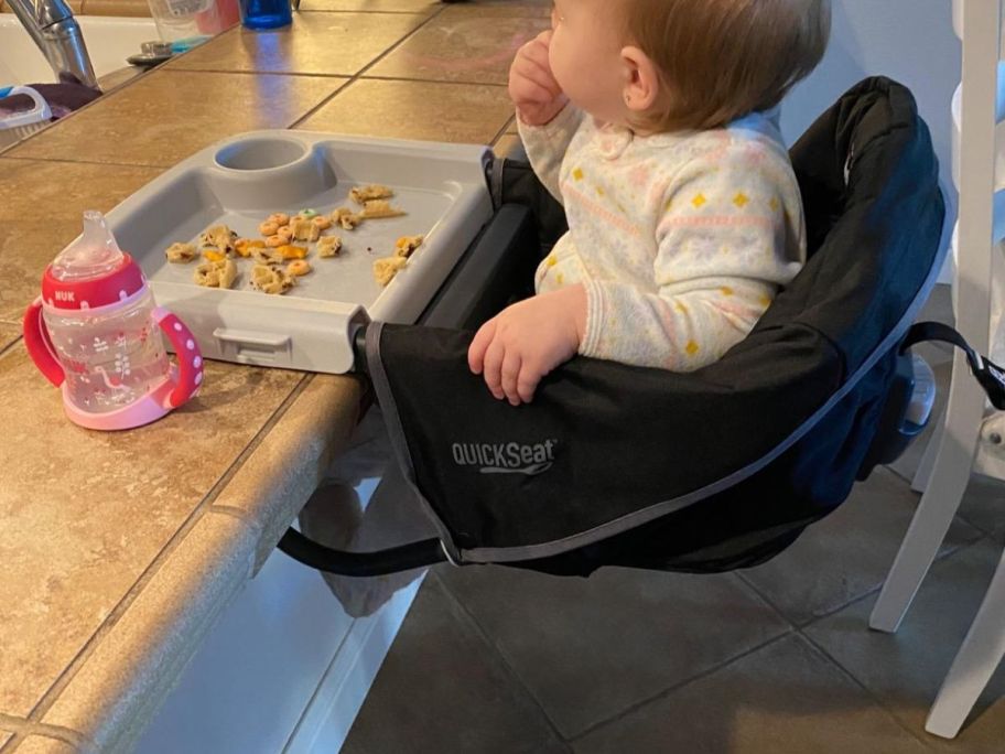 A baby sitting in a Chicco FastLock Hook-On High Chair in black in a kitchen