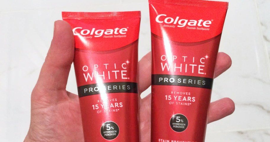 hand holding two red tubes of Colgate Optic White Pro Series Whitening Toothpaste