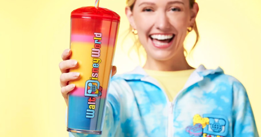 woman holding up a red, yellow, and blue disney starbucks tumbler