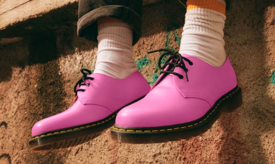 a model wearing a pair of pink dr martens lace up oxfords