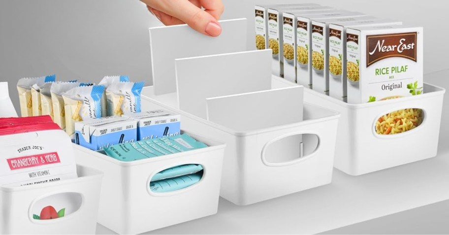 four white organizing bins with dividers, some have food items in them, woman's hand pulling dividers out of 1 