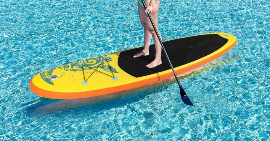 A woman standing on an orange and yellow paddle board