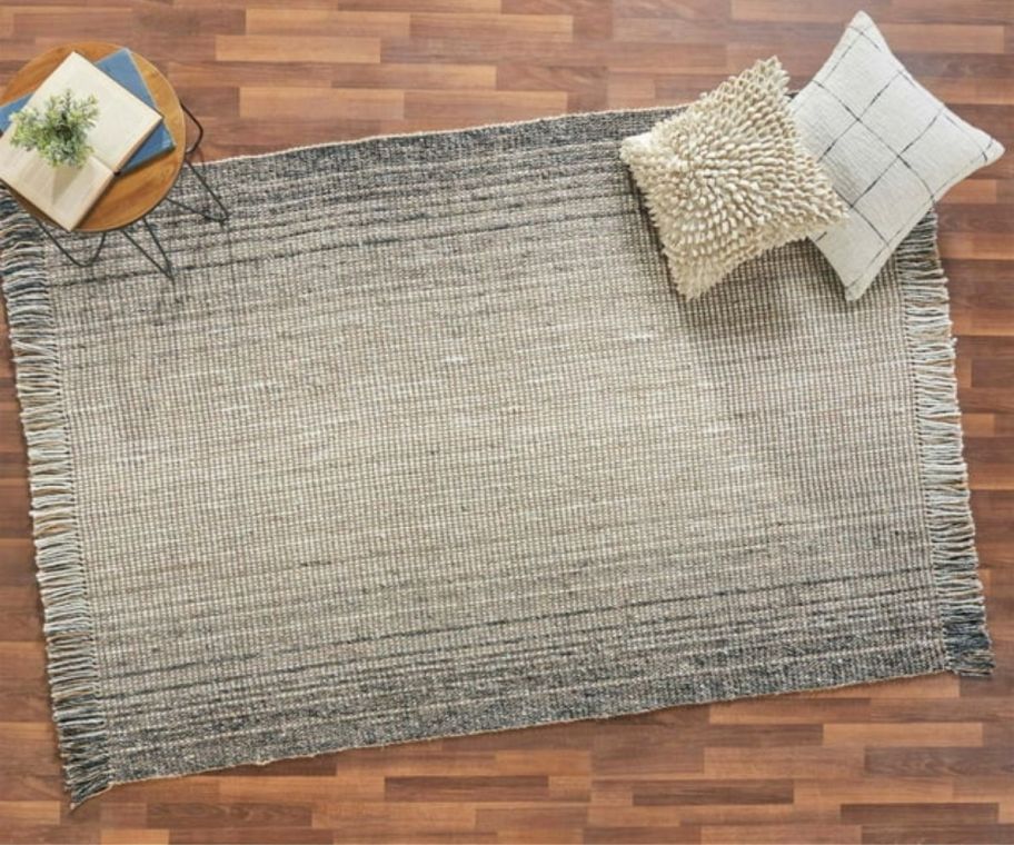 a natural colored area rug with pillows on a hardwood floor