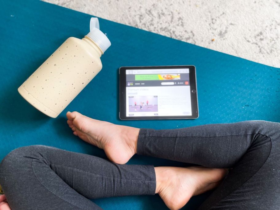 Get Healthy U TV streaming on an ipad next to a person sitting on a yoga mat