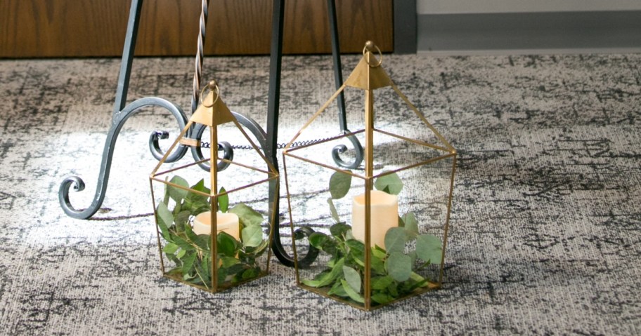 two gold lanterns on ground with eucalyptus leaves and candles