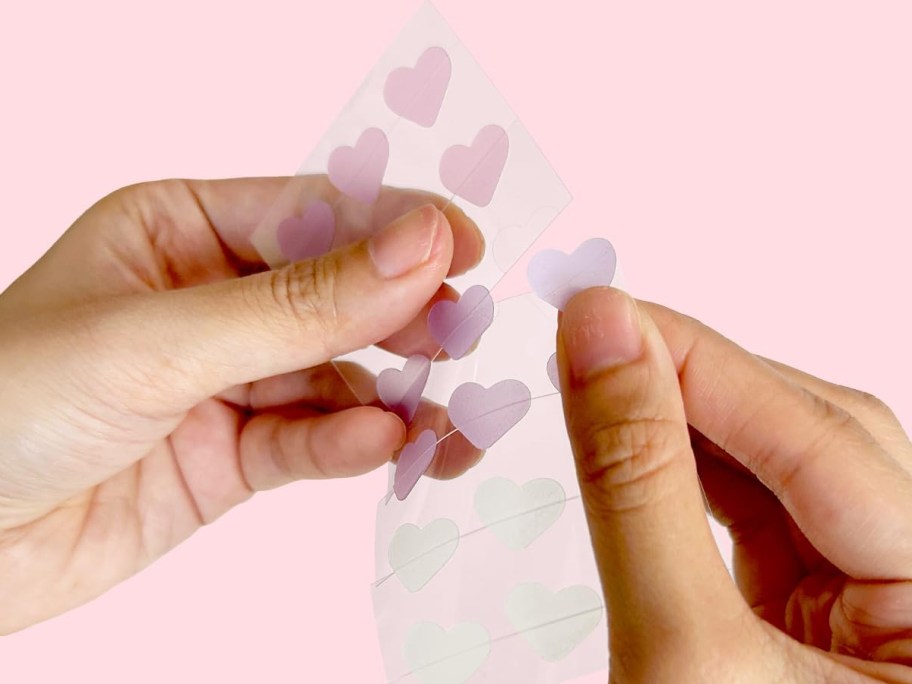 hands holding a set of heart-shaped pimple patches