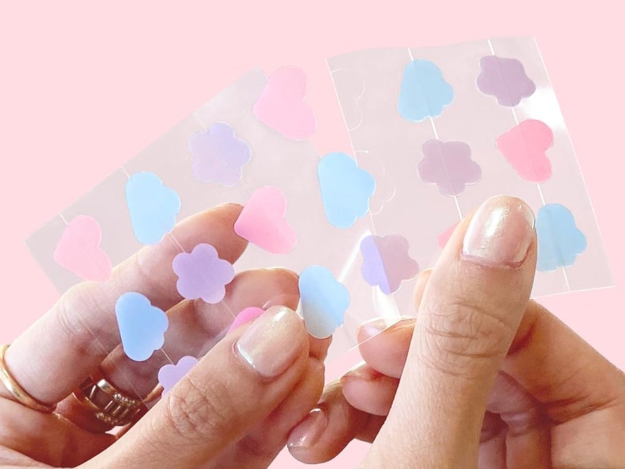 hands holding a set of cloud, heart, and flower shaped pimple patches