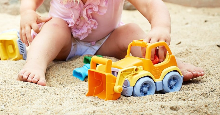 girl playing with orange and yellow construction toy in sand