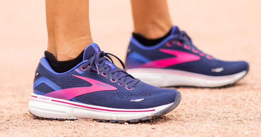 women's feet wearing blue and pink Brooks running shoes