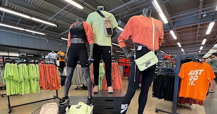 inside of a Nike store with display of mannequins wearing Nike clothes and shoes with racks of Nike clothes behind them