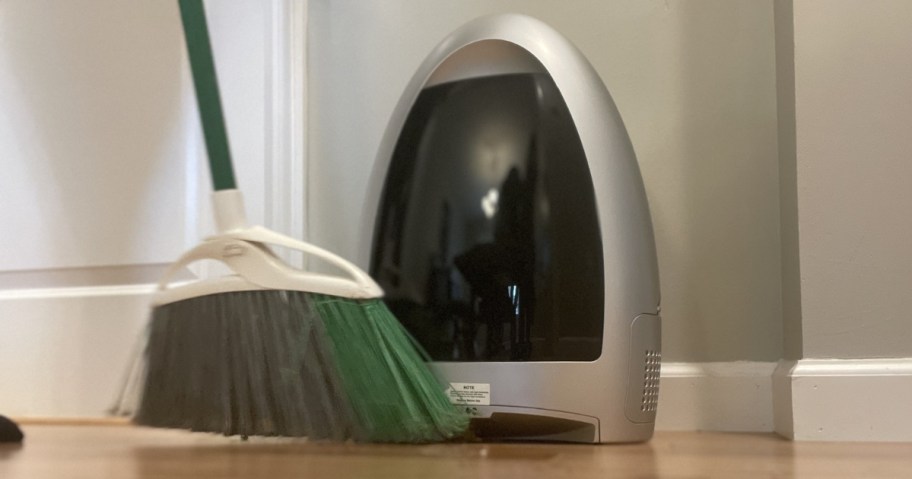 silver and black EyeVac Home Touchless Sensor Activated Vacuum with a green and white broom in front sweeping items into it
