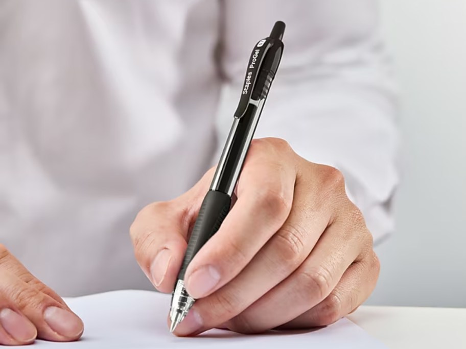 person wearing a white shirt writing in a notebook with a black ink pen