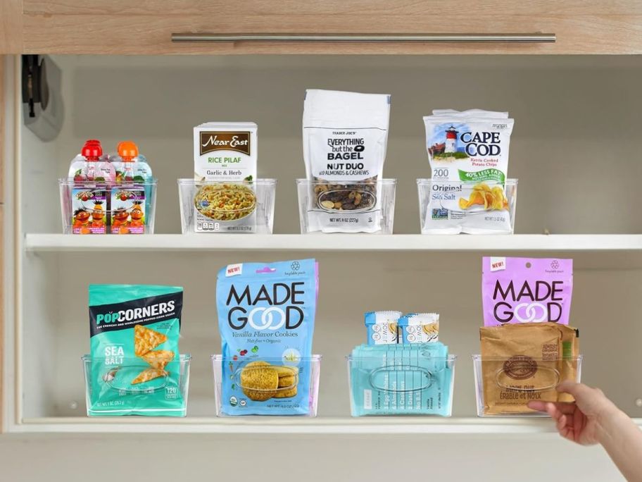 pantry shelves with clear organizing bins full of food, woman's hand reaching for 1 of them